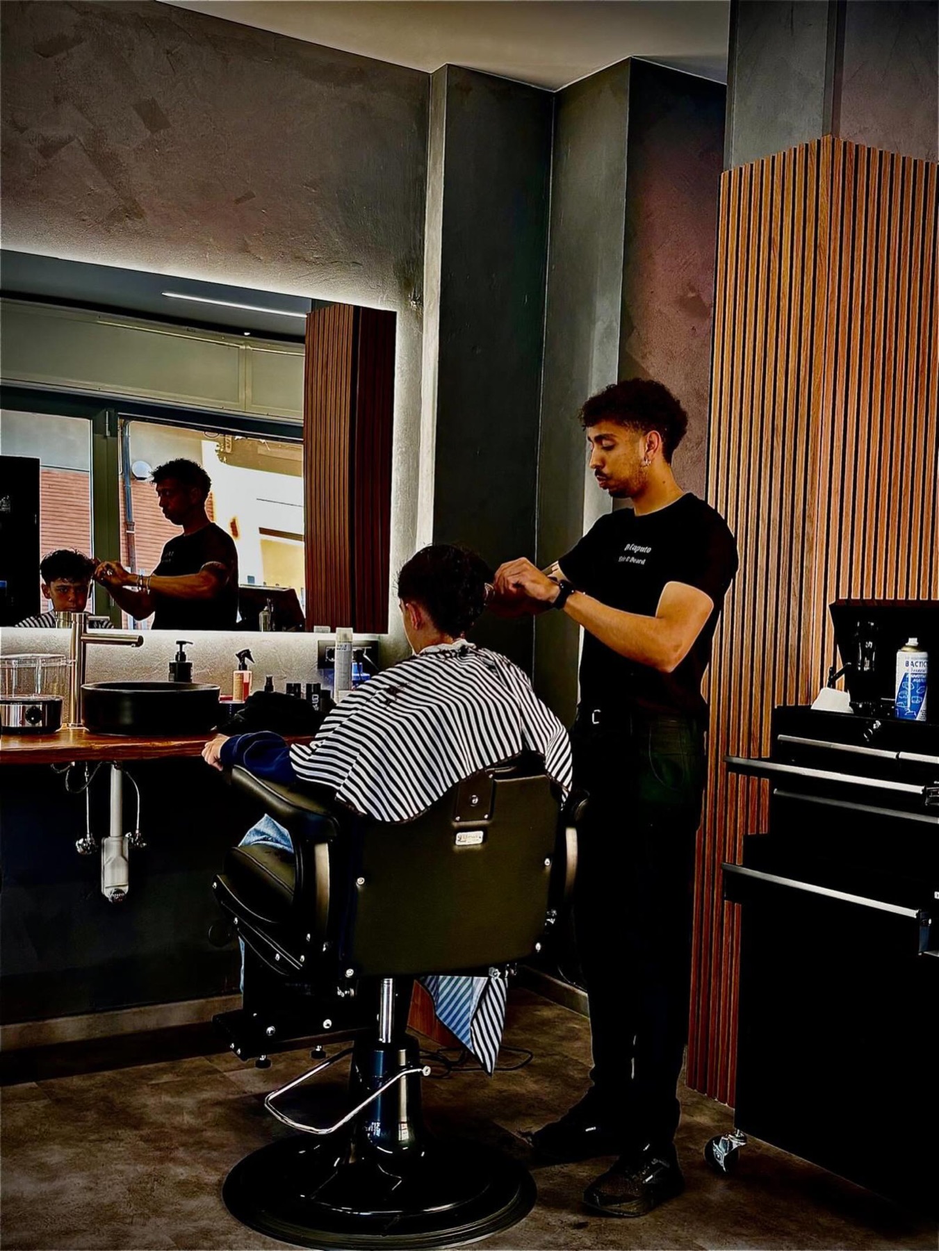 Un barber lavora su un cliente davanti allo specchio del salone