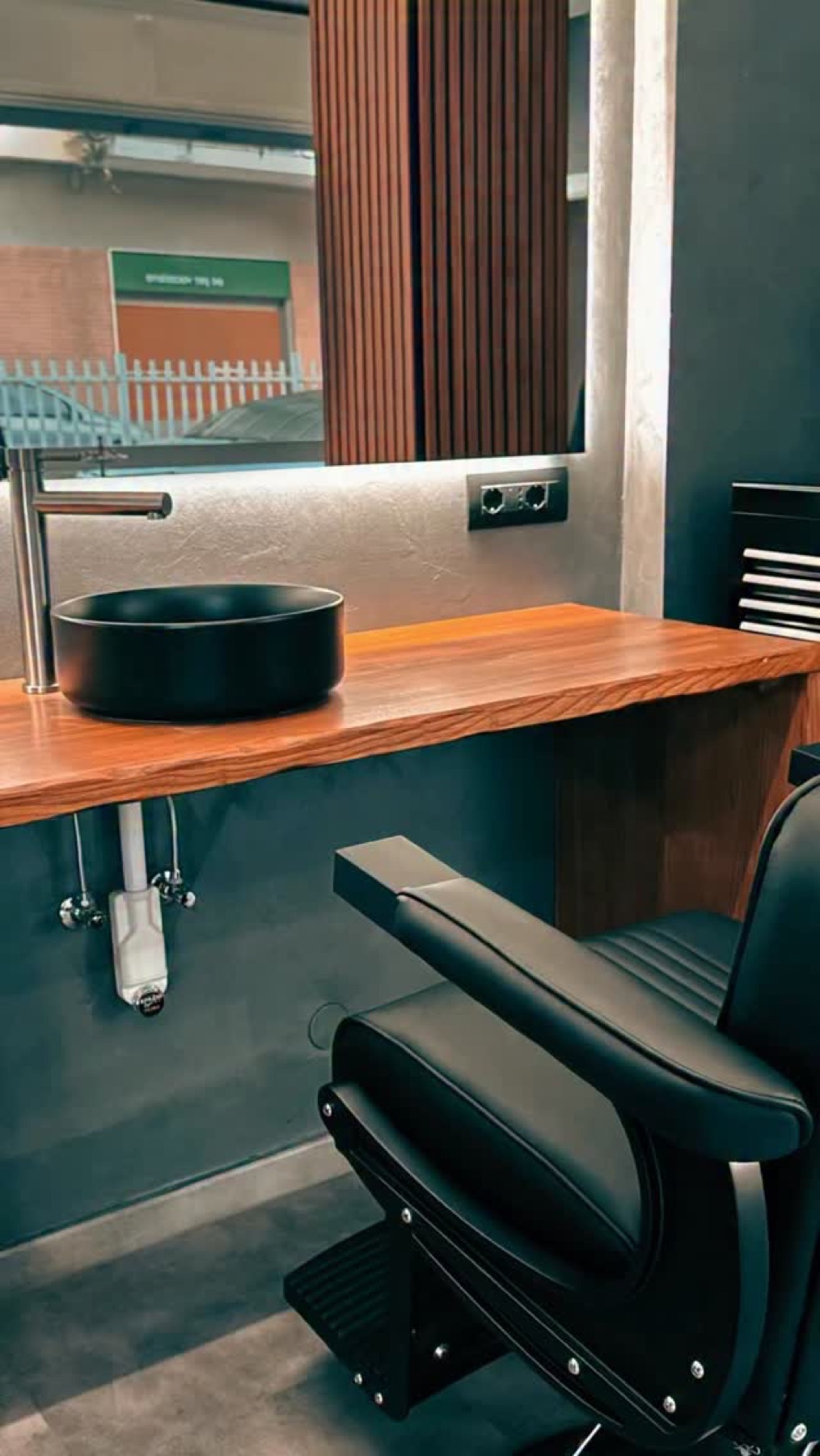 Postazione barber con poltrona nera, specchio e piano in legno